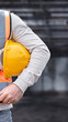 © Rawpixel.com - Person in safety gear holding a yellow hard hat at a construction site.