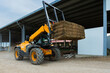 © ALIDA - Telehandler lifting hay bale in agricultural farm building