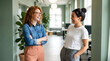 © Denspire - Two young women chatting in a modern office environment with green walls