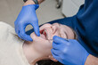 © Oksana - Dental professional in blue gloves inspecting metal braces using angled mirror and probe on teen patient reclined in chair. Overhead view of orthodontic examination with focused clinical technique....