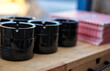 © YuliiaKettu - Stacks of glossy black ceramic ashtrays next to red checkered menus on a wooden bar counter. Great for hospitality business reviews, restaurant preparation, and catering themes.