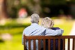 © BillionPhotos.com - Senior couple sitting on a wooden bench in a park while embracing from behind
