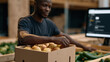 © forenna - Ugly produce subscription box being assembled in a fulfillment warehouse, a packing team member selecting misshapen apples and curved cucumbers from sorted bins while a computer
