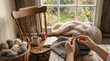 © Celso Pupo - Close-up of hands knitting a grey wool garment on a rustic wooden table with a basket of yarn, steaming coffee, and an open book in a cozy room by a window during autumn