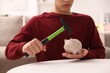 © New Africa - Man breaking piggy bank with hammer at white table indoors, closeup