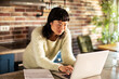 © Davor - Focused woman using laptop in home kitchen with paperwork