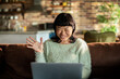 © Davor - Smiling woman waving on video call in living room