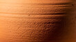 © noman.fec07 - Close-up of a textured, orange terracotta pot with horizontal lines and rough surface details in warm lighting conditions