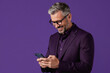 © Maryna - Mature man in suit, glasses smiles texting on smartphone. Confident businessman connects online using mobile device. Pro reads message, works remotely, enjoys conversation, chats on cell phone.