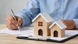 © wert - Real estate agent signing property contract, wooden house models on clipboard, home buying process, mortgage agreement, investment planning, business concept, legal documentation,