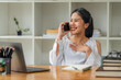 © Songsak C - Happy young Asian businesswoman talking on smartphone while working with laptop at office desk.
