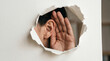© Cliff - Conceptual image of a hand placed on a human ear emerging through torn paper, representing eavesdropping, spying, communication barriers, curiosity and secrets revealed, minimalist style