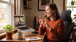 © alex - A smiling woman sits at a wooden desk making sign language hand gestures during a video call on her laptop with a man. A mug, notebook, and potted plant sit on the desk.