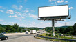 © Ardi setiawan - A large blank billboard stands on the side of a busy highway with cars and trucks driving by under a blue sky with clouds.