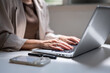 © bongkarn - Close up of a woman's hands typing on a laptop beside phone while sitting in cafe or coffee shop.
