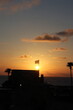 © Noa Badel - Caesarea, Israel - JUNE 2, 2026: A flag waves atop a silhouetted building against a vivid orange sunset over the ocean, with palm trees framing the scene.