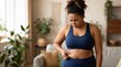 © Olga Ко - Upset plus-size African American woman in sportswear pinching belly fat at home, weight loss struggle and body image concept