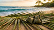 © SIMANG - Zongzi and palm leaves on a sandy beach with ocean waves and sunset sky
