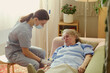 © DragonImages - Young adult female caregiver assisting senior woman receiving home care treatment with IV line, supporting eldercare and recovery. Ideal for home healthcare, nursing, caregiving marketing