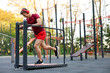 © New Africa - Young man with headphones exercising on manual treadmill at outdoor gym, low angle view. Space for text