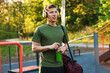 © New Africa - Young man with sports bag, headphones and bottle of water at outdoor gym