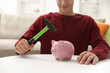 © New Africa - Man breaking piggy bank with hammer at white table indoors, closeup