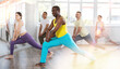 © JackF - Athletic black male instructor in blue trousers and yellow tank top leading dynamic stretching for group as part of warm-up routine before dance training session in spacious studio
