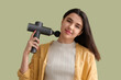 © Pixel-Shot - Young woman massaging her neck with percussive massager on green background, closeup