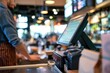 © morepiixel - A barista wearing an apron works behind a counter with a touchscreen POS system in a modern cafe or bar setting.