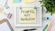 © Finasulizi - Motivational Desk Setup with Sticky Note Highlighting Progress Over Perfection on a Bright Workspace with Stationery Items