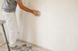 © Studio - Professional male painter sanding plaster wall with hand block during home renovation in bright indoor room, construction worker preparing surface for painting, copy space