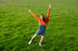 © VISTA by Westend61 - Smiling with arms raised wearing an orange shirt in a grassy field