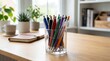 © Felippe Lopes - Desk organization with colorful pens in a glass holder, notebook, and potted plants by the window