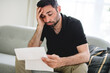 © Louis-Paul Photo - Depressed mature man holding paper and looking at it while sitting on the couch at home