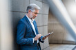 © Westend61 - Mature businessman standing at a wall using tablet