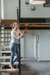© Westend61 - Smiling woman controlling home functions with smart phone while standing on steps at home