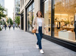 © Hikmat Ullah  - Young woman walking on a city sidewalk past a modern clothing boutique