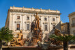 © Travel 'n' Lifestyle - View of the Fountain of Diana with its intricate sculptures in front of the historic Banco di Sicilia building under a clear blue sky in Syracuse, Sicily, Italy.