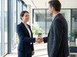 © Afdal - A smiling businesswoman and man shake hands in a modern office lobby with large windows.