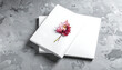 © men - Stack of blank white open books with a single vibrant red and pink autumn leaf resting on the pages, set against a textured grey background with scattered glitter.