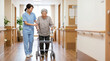 © Xenia - Japanese nurse helping an elderly woman walk with a wheeled walker in a nursing home. Smiling caregiver assisting a senior patient in a corridor