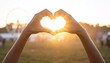 © SolaruS - Hands making a heart shape against a glowing golden sunset at an outdoor summer festival with a blurred Ferris wheel in the background. Ideal for themes of love, youth, and hope.