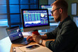 © New Africa - Financial trading specialist with paper cup of coffee working on laptop at desk in office