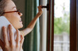 © SHOTPRIME STUDIO - Smiling woman with glasses on a phone by a window, bright natural light, cozy home setting, calm mood, clear lifestyle moment focusing on connection and daily routine