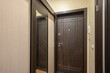 © evgeniykleymenov - narrow hallway with beige textured wallpaper, dark wood sliding wardrobe with mirror, matching entrance door, tiled floor, and intercom system
