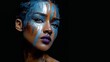© Evarelle - Close up portrait of woman with metallic blue face paint. Artistic makeup with silver streaks and purple lips on black background. Creative fashion photography