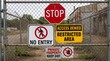 © Vendi - Multiple warning signs on a chain link fence: Stop, No Entry, Restricted Area, and Private Property Keep Out.
