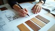 © Pete - Architect draws building plan near wood samples. Designer selects material for home renovation project. Person works on blueprint with color swatches.