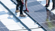 © Preethiloki - Multiple worker using drill to fasten solar panel row on bright rooftop