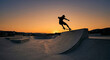 © Jana - The distinct silhouette of a skateboarder performing a trick on a concrete ramp is captured against a warm, vibrant orange sunset at a skatepark.